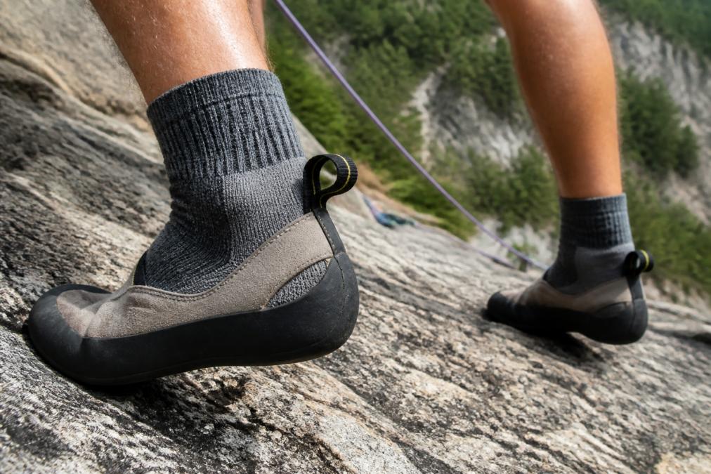 Climber's feet showing proper sock coverage during granite multi-pitch route, demonstrating friction points at heel collar and toe box where blisters typically form