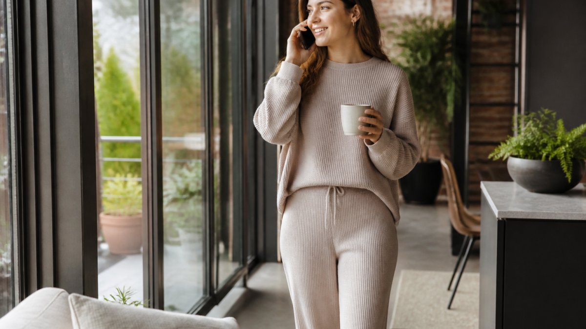A woman in soft rib-knit lounge pants and a waffle-knit pullover sitting on a couch, holding a mug, with the fabric's structured drape and shape clearly visible in natural light