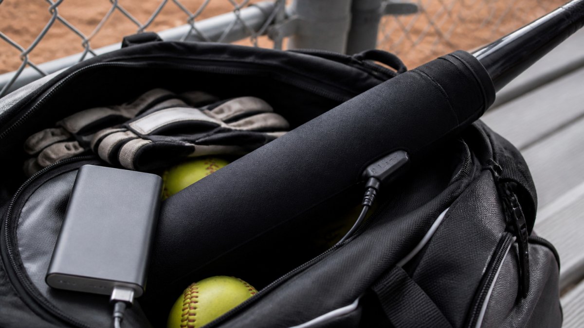 Softball bat with a heated thermal sleeve and portable power bank stored inside an equipment bag for cold weather play