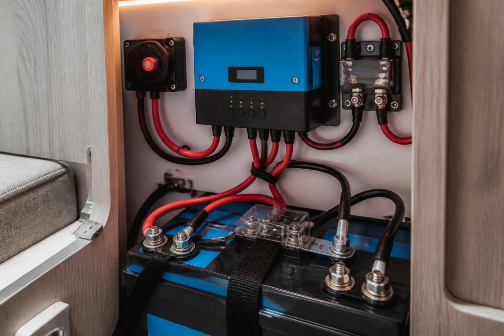 Close-up of a solar charge controller mounted in a campervan electrical cabinet with lithium battery terminals, wiring, and a small display screen visible