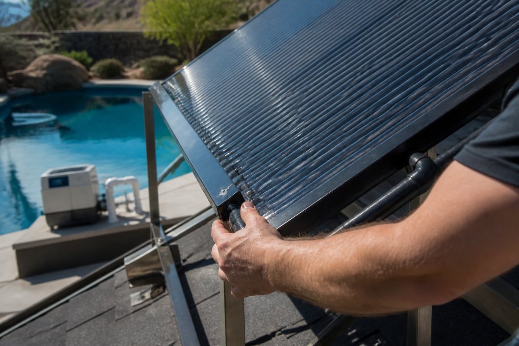 Technician inspecting a solar pool heater panel next to a residential salt chlorine generator system