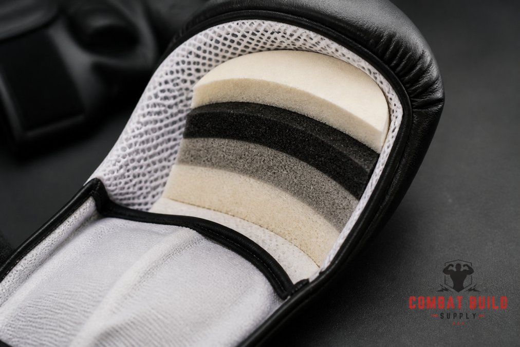 Close-up of multi-layered foam padding structure inside competition sparring glove, showing protective cushioning layers and breathable mesh lining with professional lighting