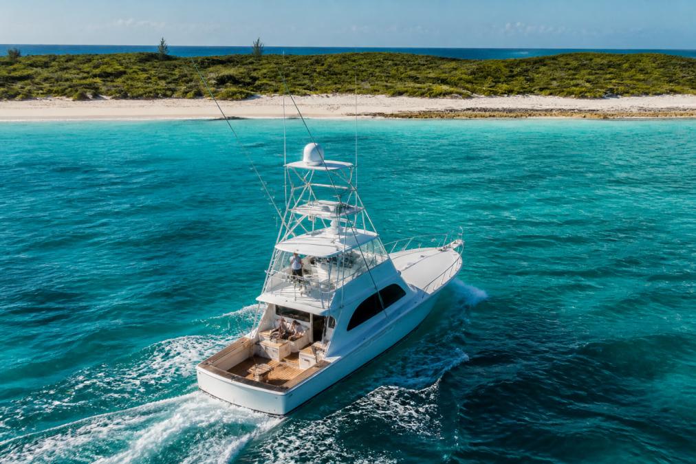 A sleek sportfish yacht cruising through turquoise Bahamian waters with a white sand beach in the distance.