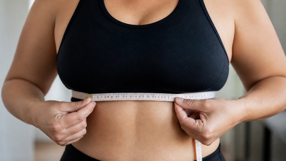 Hands holding a soft tape measure wrapped snugly around the ribcage to determine bra band size