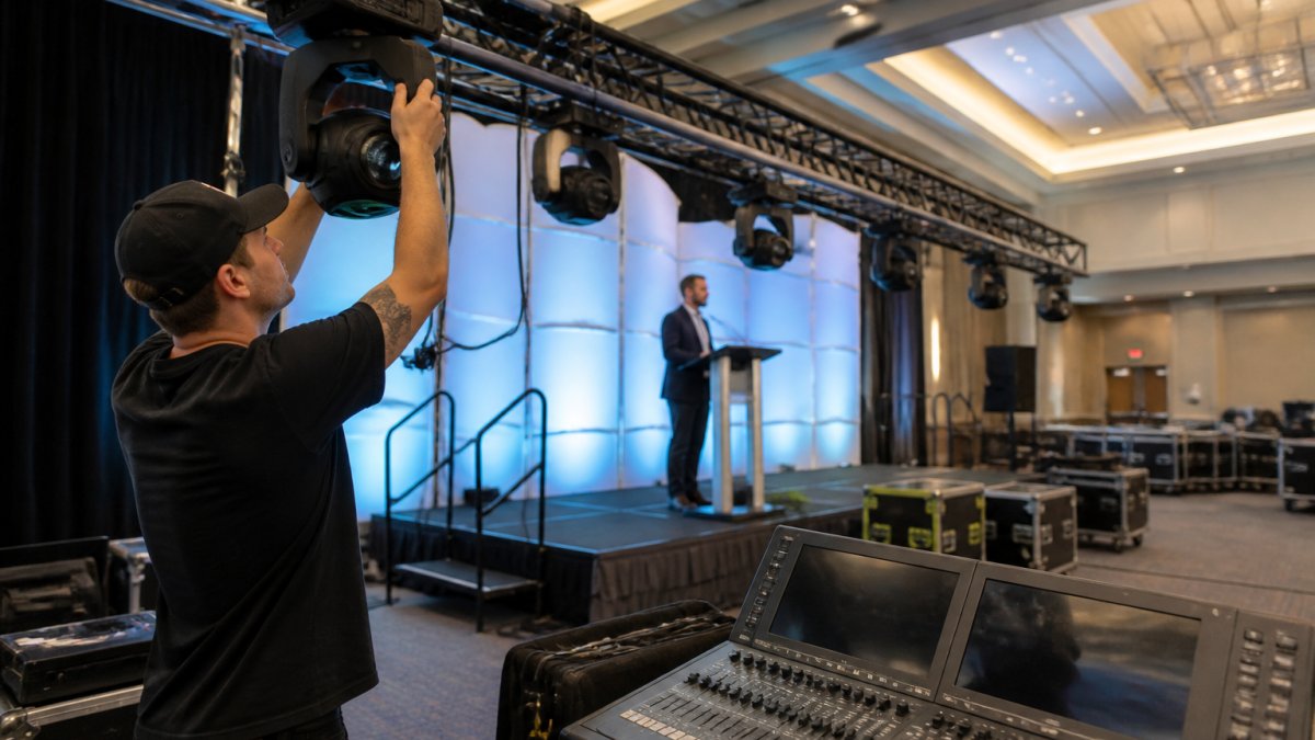 Technician adjusting a stage lighting fixture above a presenter at a corporate podium