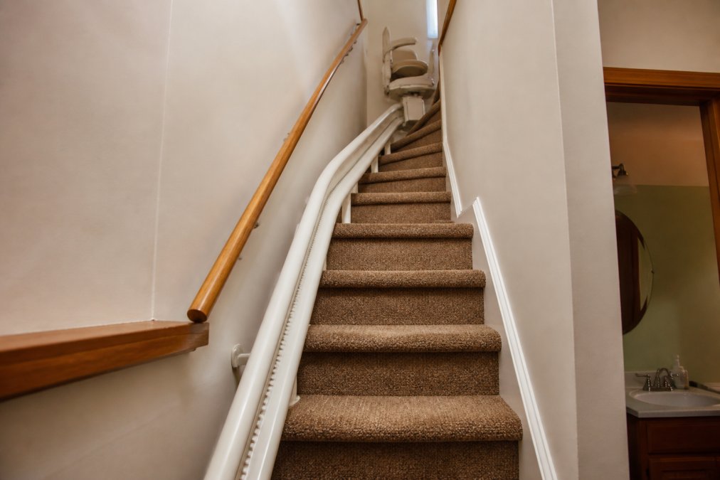A residential staircase with a steep incline and a narrow landing, viewed from the bottom, showing the challenging geometry of a curved rail installation