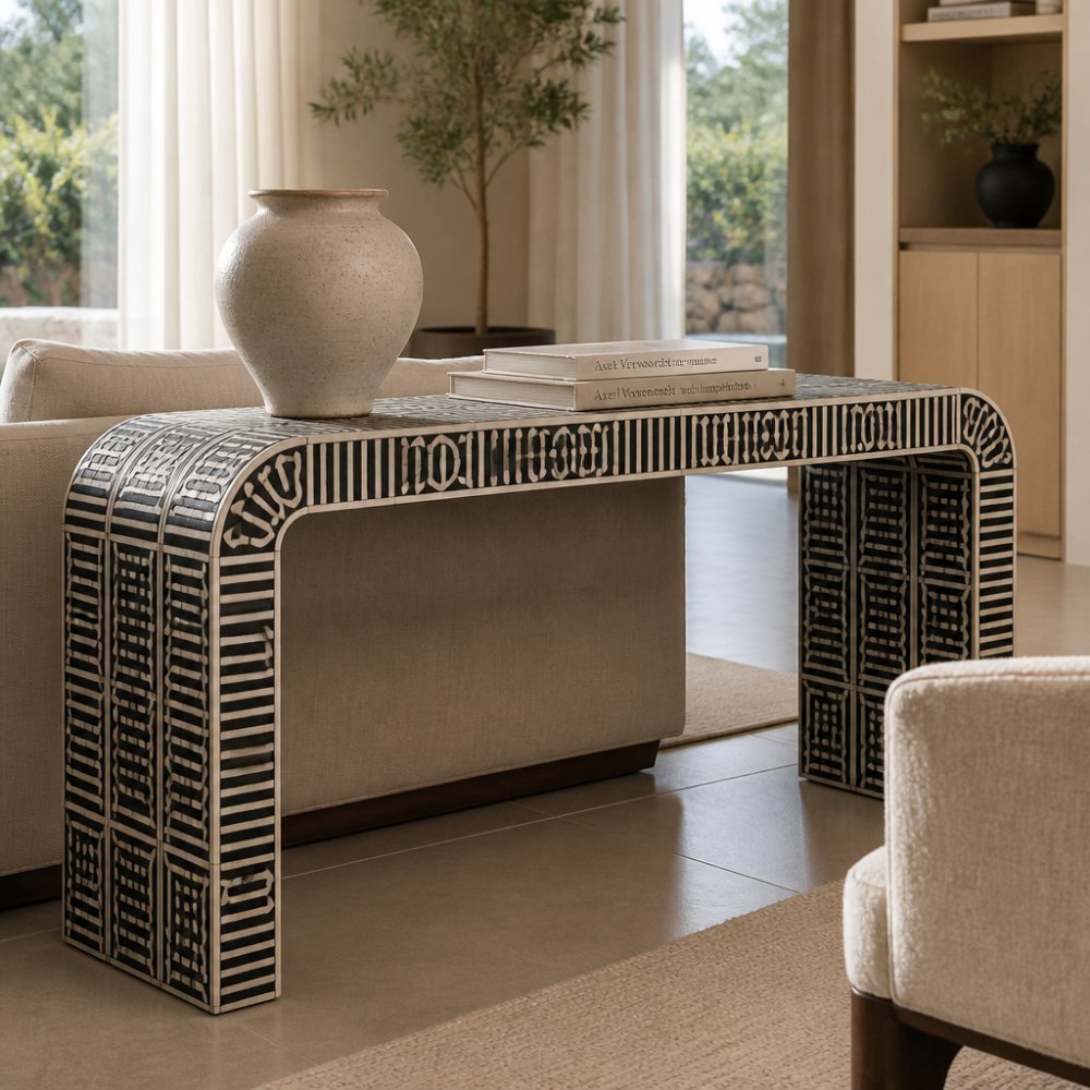 Modern living room featuring a sculptural black and white bone inlay console table as the focal point, styled with a single ceramic vessel and stacked books, warm natural light streaming through large windows, neutral furnishings creating a curated aesthetic