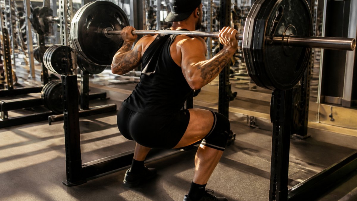 Athlete performing barbell back squat with proper form and depth in well-equipped gym with bright lighting, focusing on lower body strength and proper knee tracking