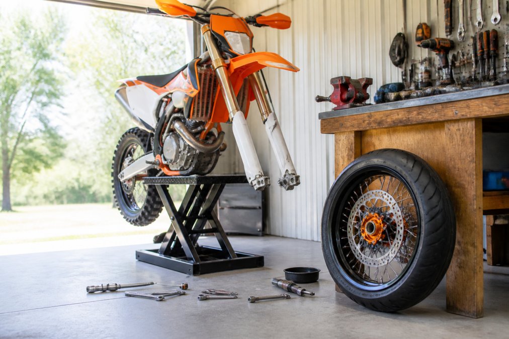 KTM dirt bike on a lift with a new 17-inch supermoto wheel set ready for installation in a sunny garage