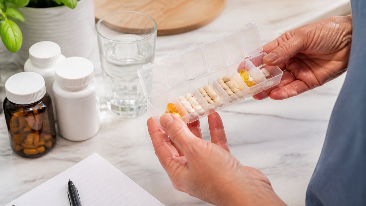 Hands holding a weekly pill organizer with tablets for the best supplements for chronic fatigue on a kitchen counter