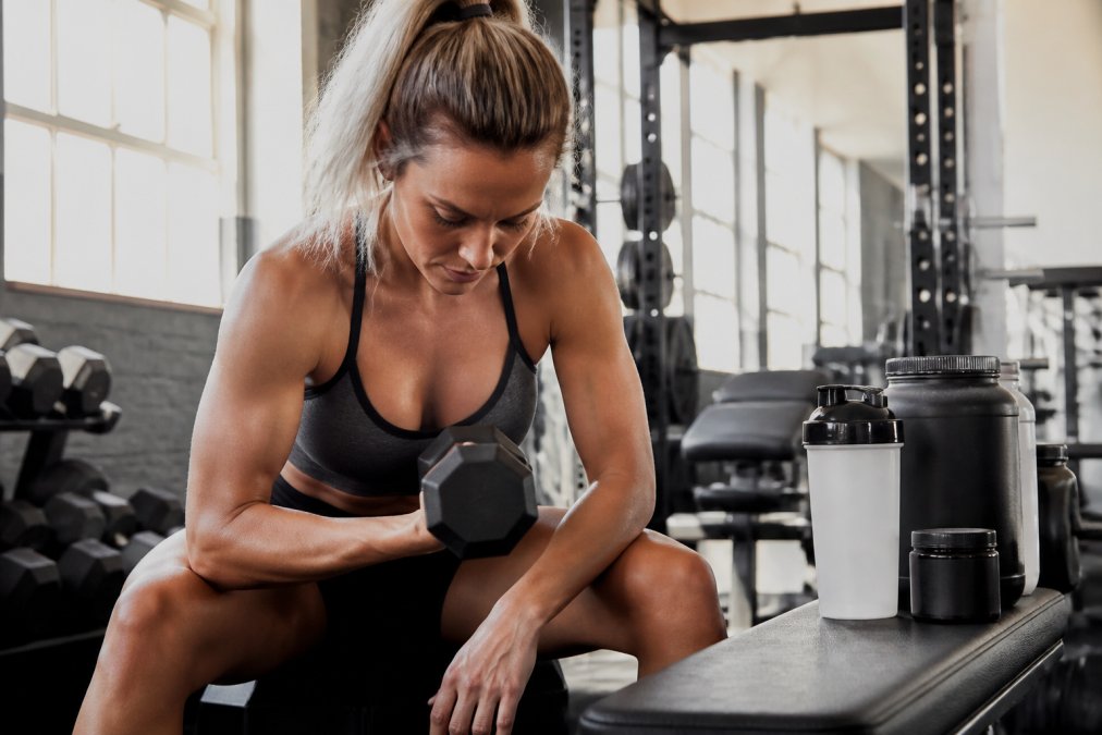 Fit woman lifting dumbbells in a gym with supplements for women nearby
