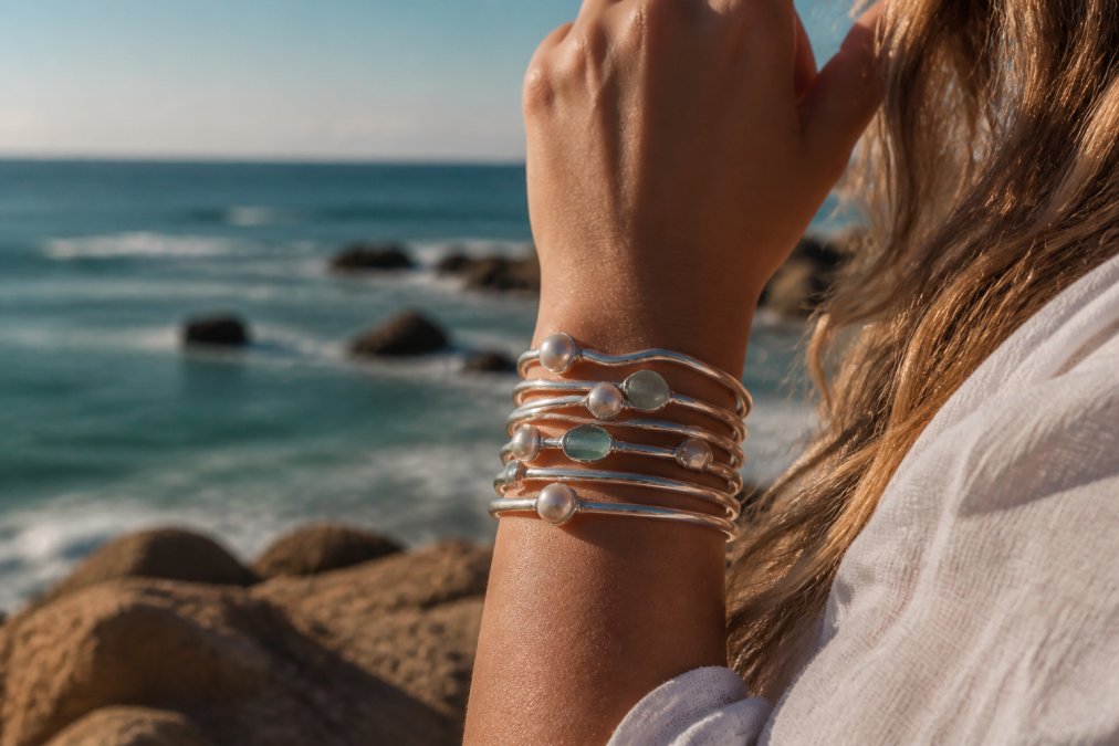 Woman wearing handmade sterling silver sustainable jewelry bangles with pearls and sea glass by the ocean.