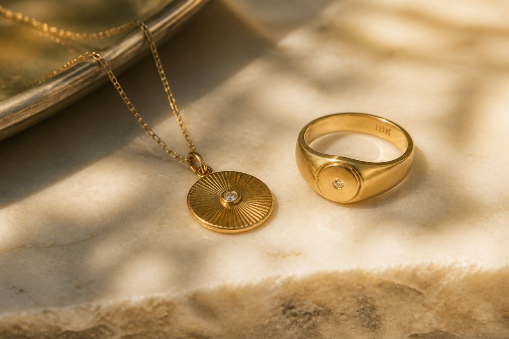 Close-up of an 18k gold ring and pendant resting on a marble surface, warm natural light highlighting the texture and hallmark stamp on the metal