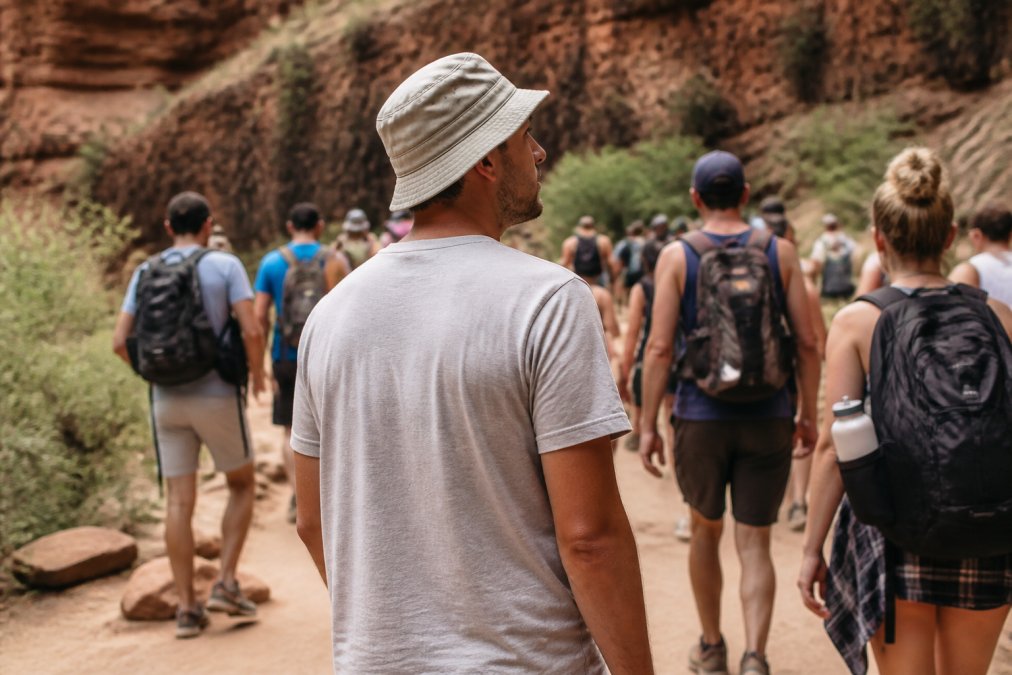 Person in casual clothing and a bucket hat hiking among a crowd, blending tactical gear into an everyday look.