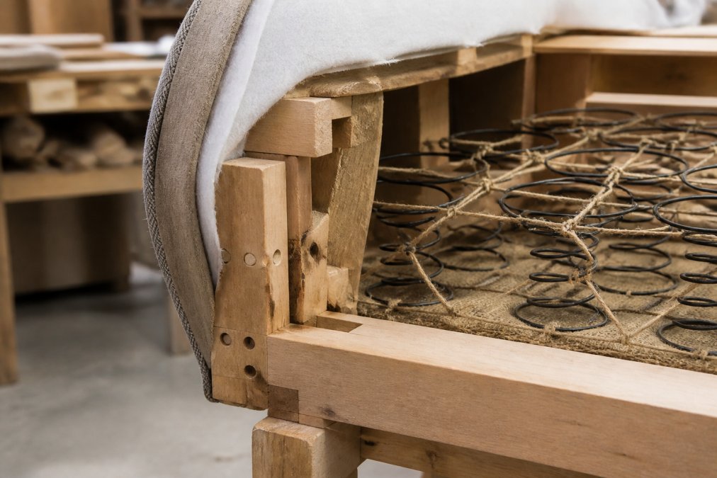 Close-up of exposed hardwood frame construction showing hand-built joinery and coil-sprung suspension system beneath upholstery fabric in a furniture workshop