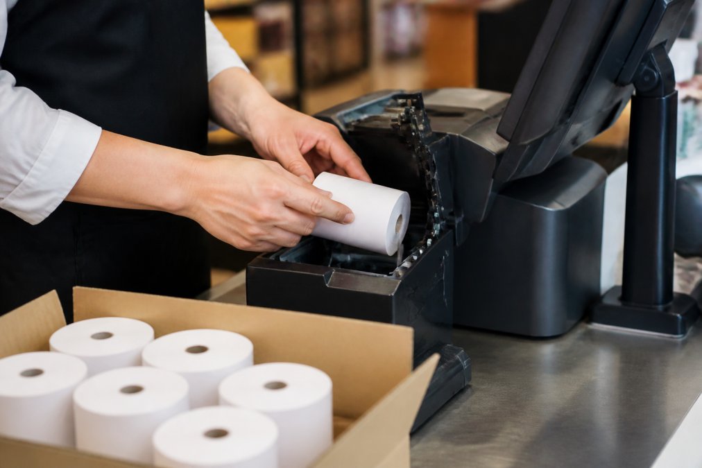 Shop assistant loading a fresh thermal paper roll into a modern retail EPOS terminal at a checkout counter