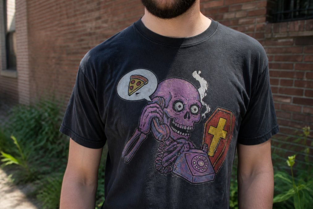 Close-up of a person wearing a retro-style graphic t-shirt with a bold, hand-drawn humorous design, standing in a casual urban setting with natural light