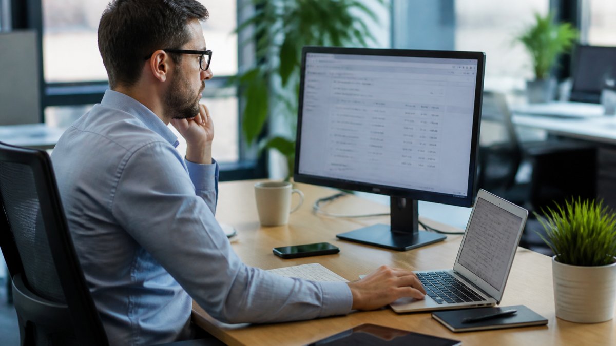 Finance professional reviewing bank transactions and account balances on a computer screen in a modern office environment with natural office lighting