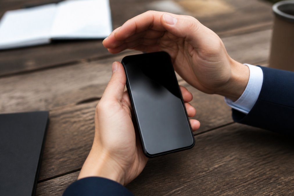 Close-up of hands protecting a smartphone displaying sensitive property inspection data on screen, with a padlock icon visible, professional office setting