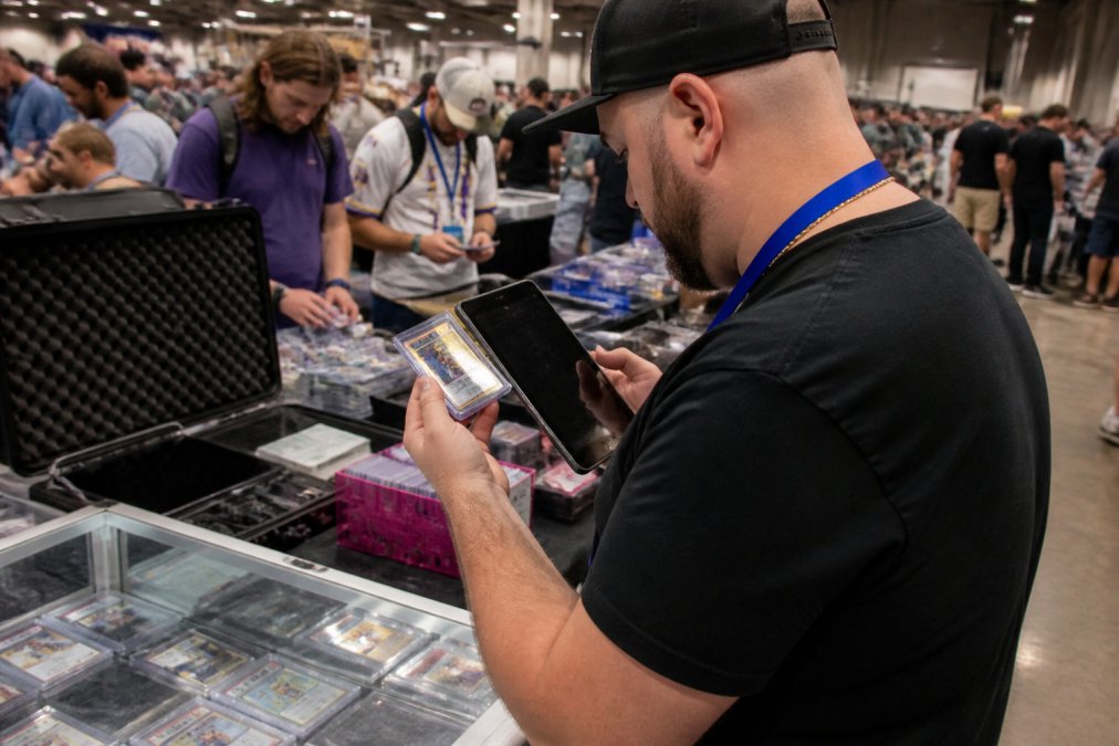 Vendor using a trading card app on an iPad to scan a collectible sports card at a busy hobby show booth
