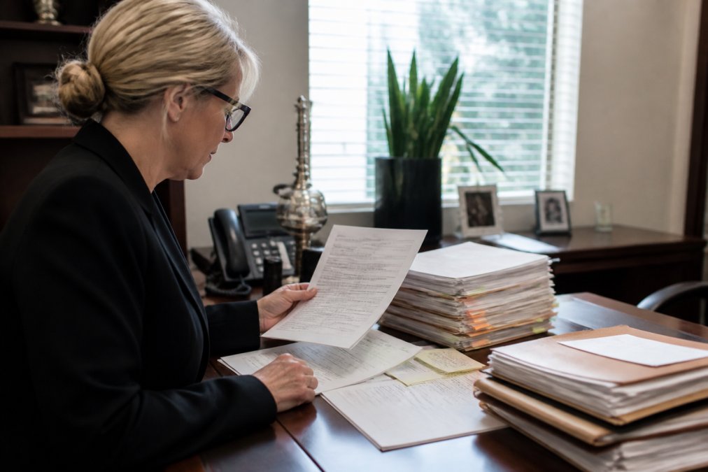Paralegal professional working at desk reviewing property deeds and title documents on computer screen displaying title search results in modern office setting