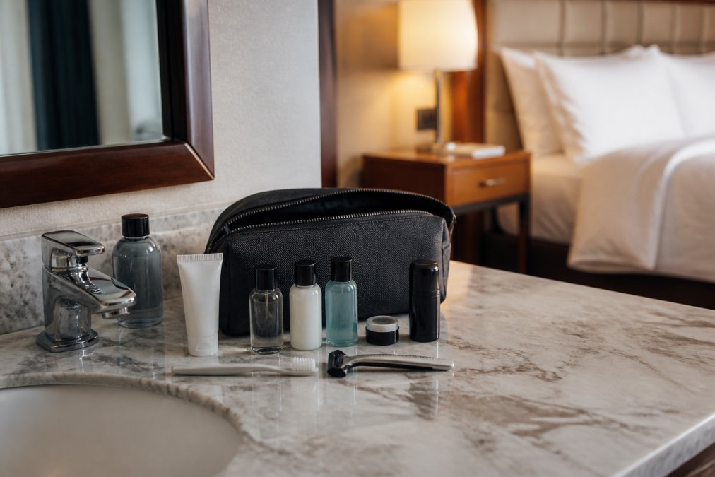 Business traveler unpacking a compact grooming kit on a marble hotel bathroom counter in warm morning light.