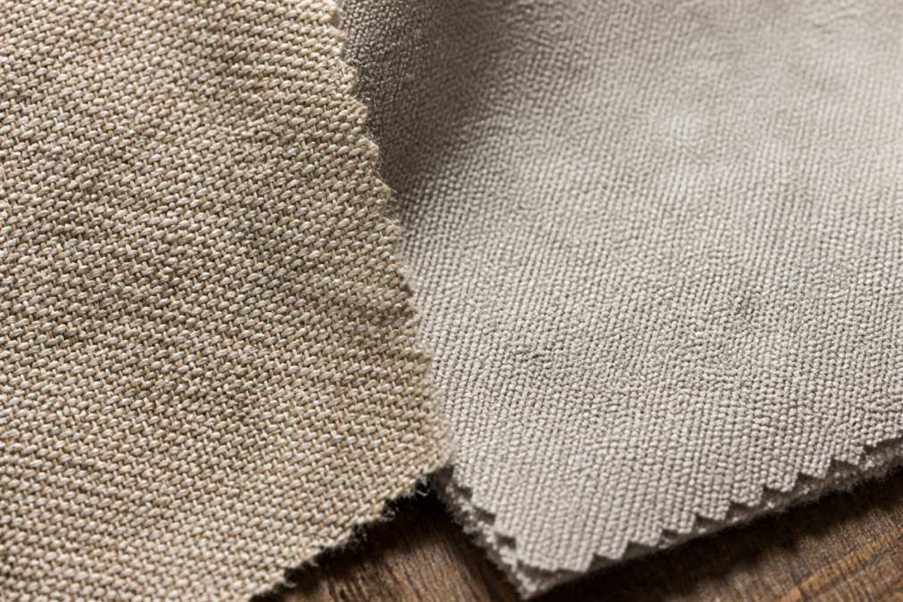 Close-up of fabric swatches showing texture differences between natural linen weave and synthetic polyester blend under natural light, highlighting weave structure and pile density variations