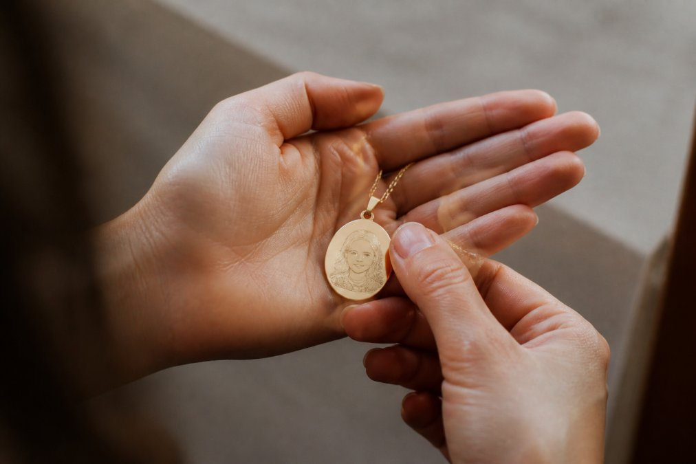Hands holding a personalized piece of jewelry with detailed engraving visible, displayed against soft neutral background showing the quality and customization of hand-finished domestic craftsmanship