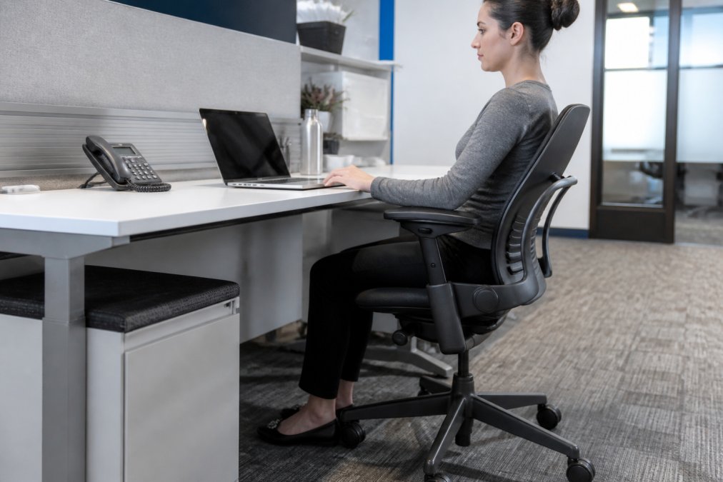 Professional office workspace with a used Steelcase Leap V2 chair positioned at a workstation showing proper ergonomic posture, lumbar support, and adjustable armrests with natural office lighting