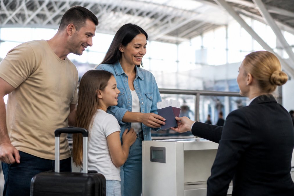 A happy family with a suitcase and passports smiling at an airport check-in counter, natural light, travel excitement
