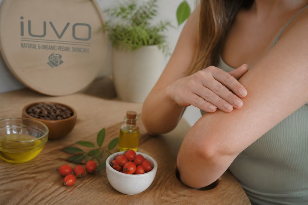 Close-up of a person with sensitive skin gently applying a plant-based oil to their arm, with natural ingredients like jojoba and rosehip visible in the background on a wooden table