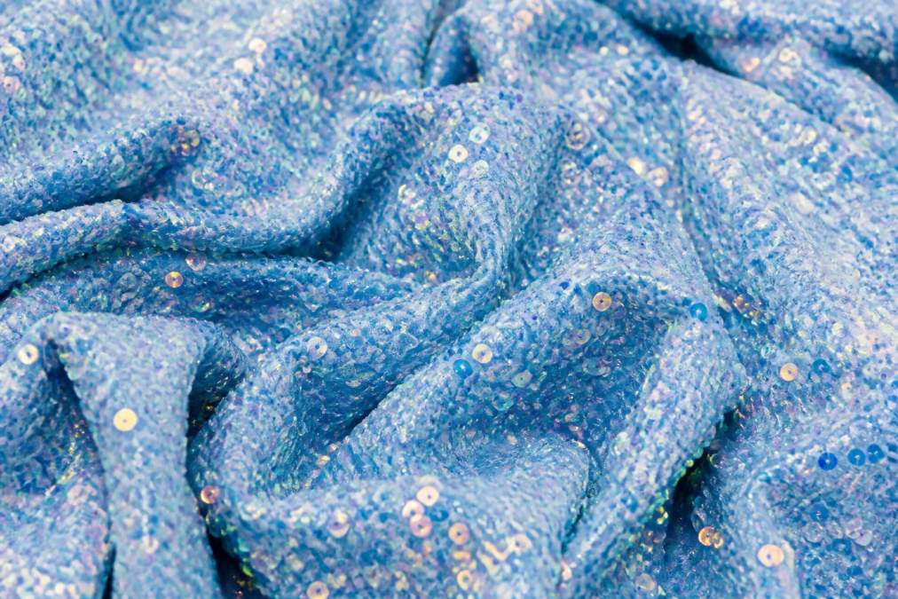 Close-up of sequin velvet fabric catching directional light, showing iridescent sparkles and shimmering highlights with visible depth of pile texture and individual sequin reflection