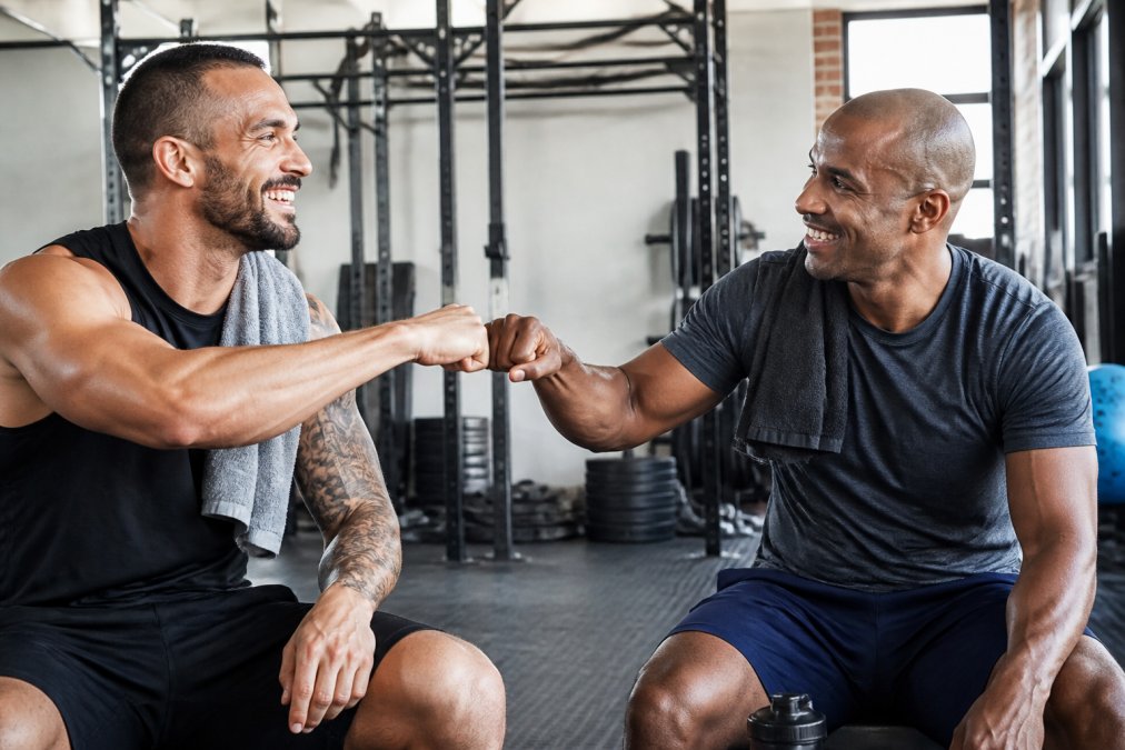 Two veterans in workout gear giving each other a fist bump after a training session in a well-lit gym, both smiling and energized, fitness equipment visible in background