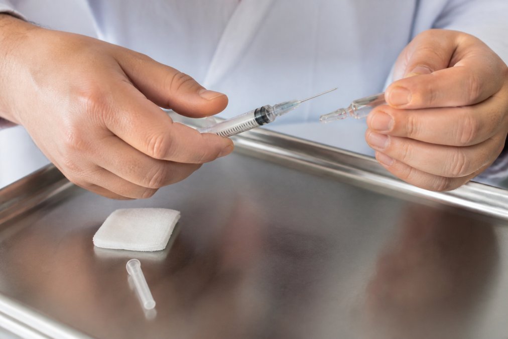 Hands preparing a vitamin b6 injectable ampule and syringe on a sterile tray with an alcohol swab nearby