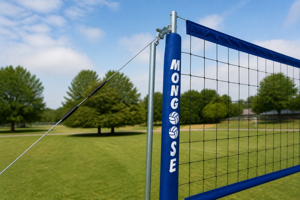 Close-up of a volleyball net being set up outdoors on grass, showing the net tensioning system and aluminum posts with guy lines clearly visible, natural daylight