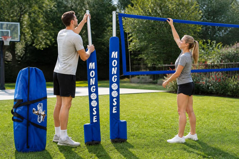 Two people quickly assembling a portable volleyball net system in a backyard, one adjusting the telescoping poles while the other guides the net into position, showing tool-free setup and ease of use in afternoon sunlight