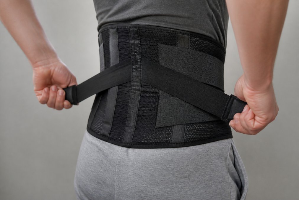 Hands adjusting the dual-pull straps of a waist support belt around the lower back for a snug fit