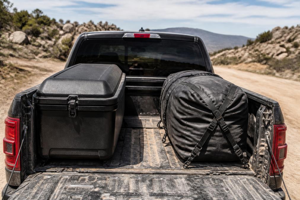 Fully loaded truck bed with hard-shell fiberglass cargo box mounted on one side and waterproof soft cargo bag secured with ratchet straps on the other, both during off-road adventure in dusty terrain