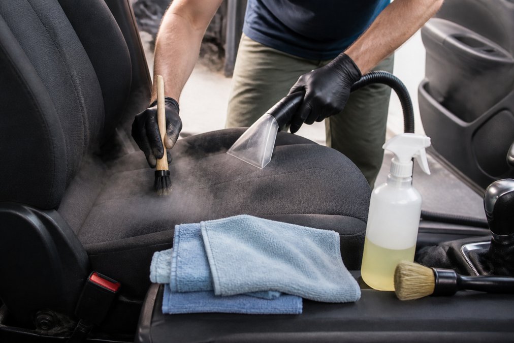 Person wearing gloves using a steam cleaner and brush to remove car odors from a cloth seat