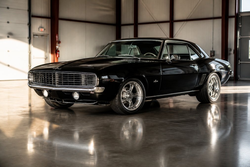 Pristine classic car positioned at a three-quarter angle in a well-lit garage, dramatic side lighting accentuating the vehicle's curves and chrome details, polished concrete floor reflecting the body