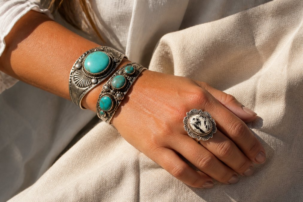 Close-up of a woman's wrist and hand wearing two stacked sterling silver turquoise cuffs and a bold oval statement ring, resting on natural linen fabric in warm afternoon light