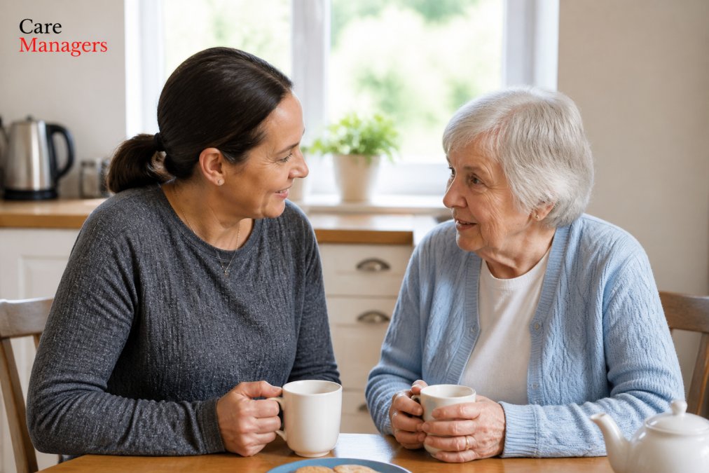 An adult daughter sitting at a kitchen table having a gentle, warm conversation with her elderly mother over tea, soft natural light through the window