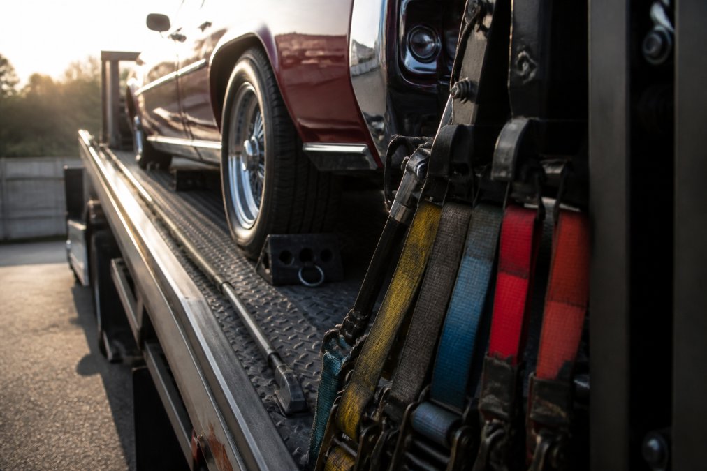 Close-up of professional towing equipment including color-coded soft-tie straps, hydraulic lift gate mechanism, vehicle wheel chocks, and securement rails on a flatbed truck bed in daylight