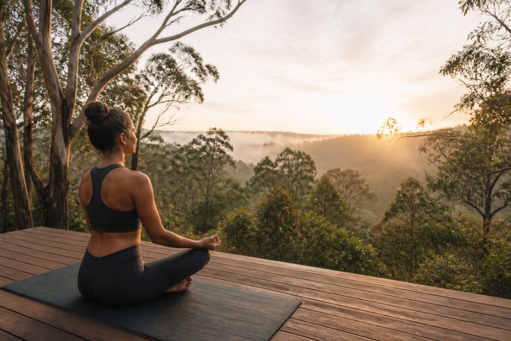 Woman practicing yoga on a misty forest deck at sunrise during wellness retreats in Tasmania.