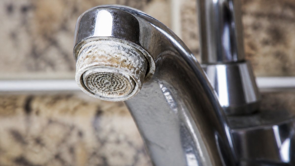 Diagram showing mineral scale buildup on faucets caused by hard water, signaling a need for a whole home water softener.