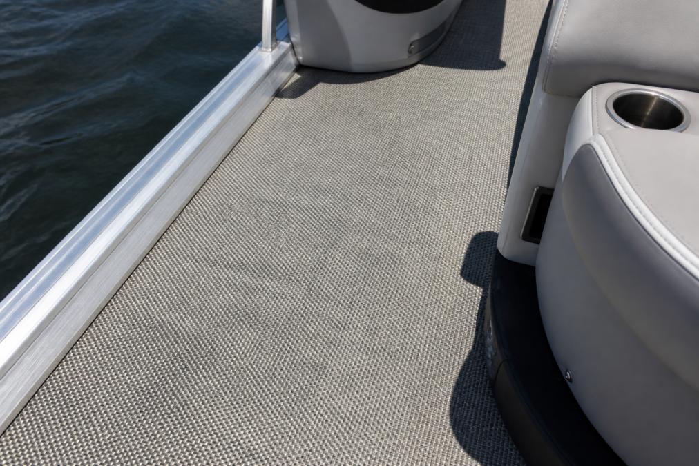 Close-up of a pontoon boat deck covered in woven vinyl flooring, showing the textured surface and clean edges against aluminum rails under bright sunlight
