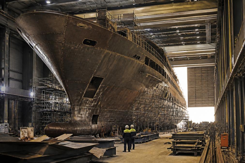 Workers and scaffolding surround a custom superyacht hull at one of the best yacht builders for custom projects.