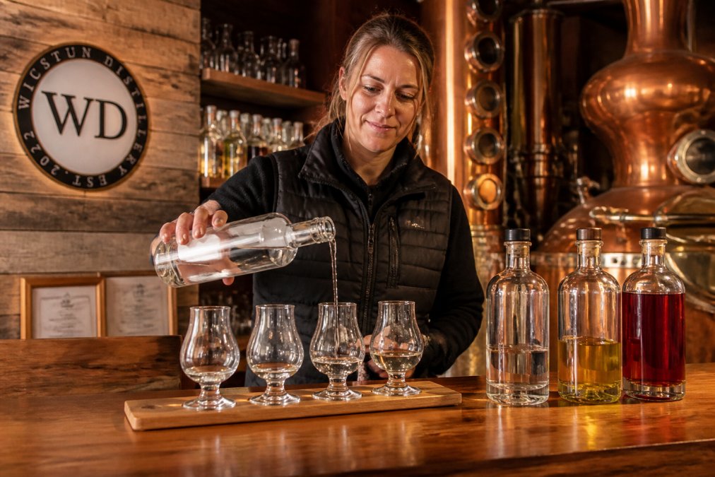 Distillery expert pouring artisanal gin into crystal glasses at a warm wooden bar counter