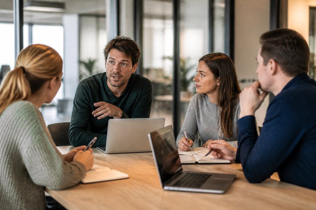 Team van webprofessionals in overleg rond een tafel met laptops en notitieblokken, discussie over conversie-optimalisatiestrategie in modern kantoor