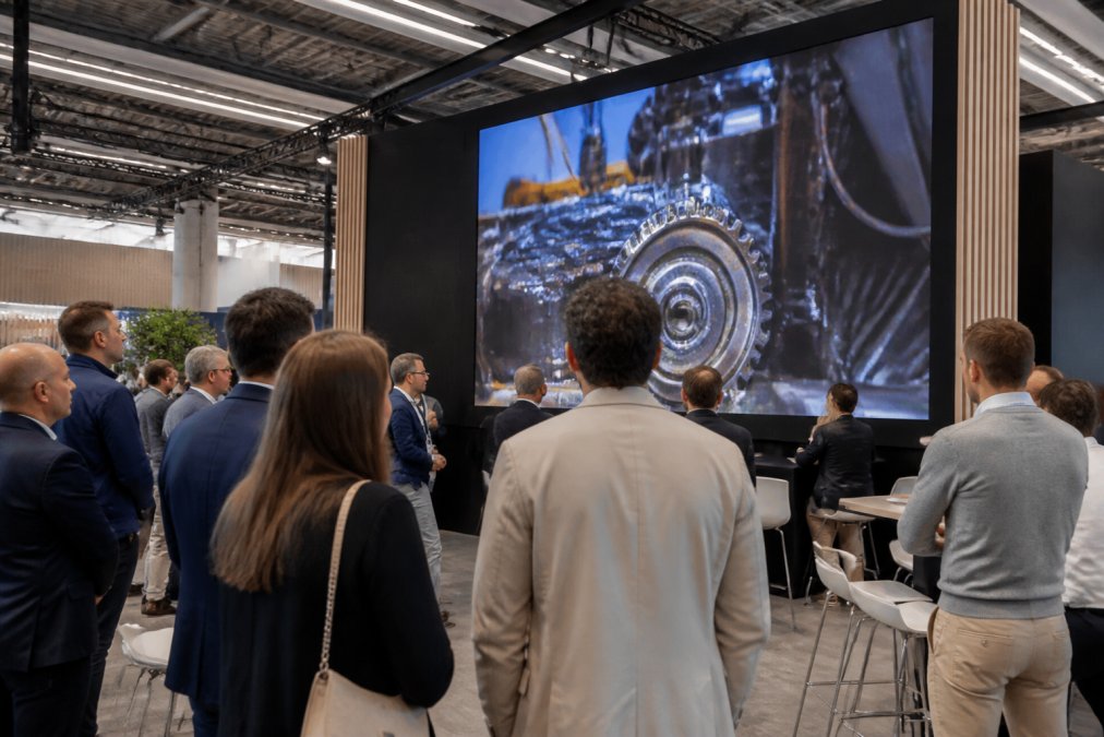 Een moderne beursstand met een groot LED-scherm waarop een productvideo wordt getoond, omringd door bezoekers die het scherm bekijken
